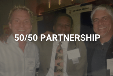 The words "50/50 Partnership" are across the image in white. Three men are joined at the shoulders, smiling for the photo. They are dressed in business casual suits and have name tags on their right side chest plate.
