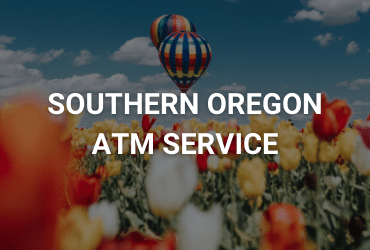 The words "Southern Oregon ATM Service" are across the image in white. In the foreground are blurry tulips in red, white, and yellow. In the background is a vibrant, colorful, stripped hot air balloon.
